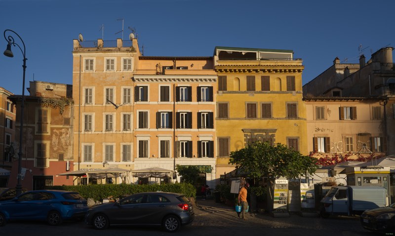 A man in orange walks by a row of Roman restaurants in the summer sun.